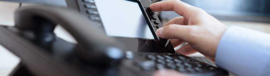 Eine Hand tippt auf einem Festnetztelefon